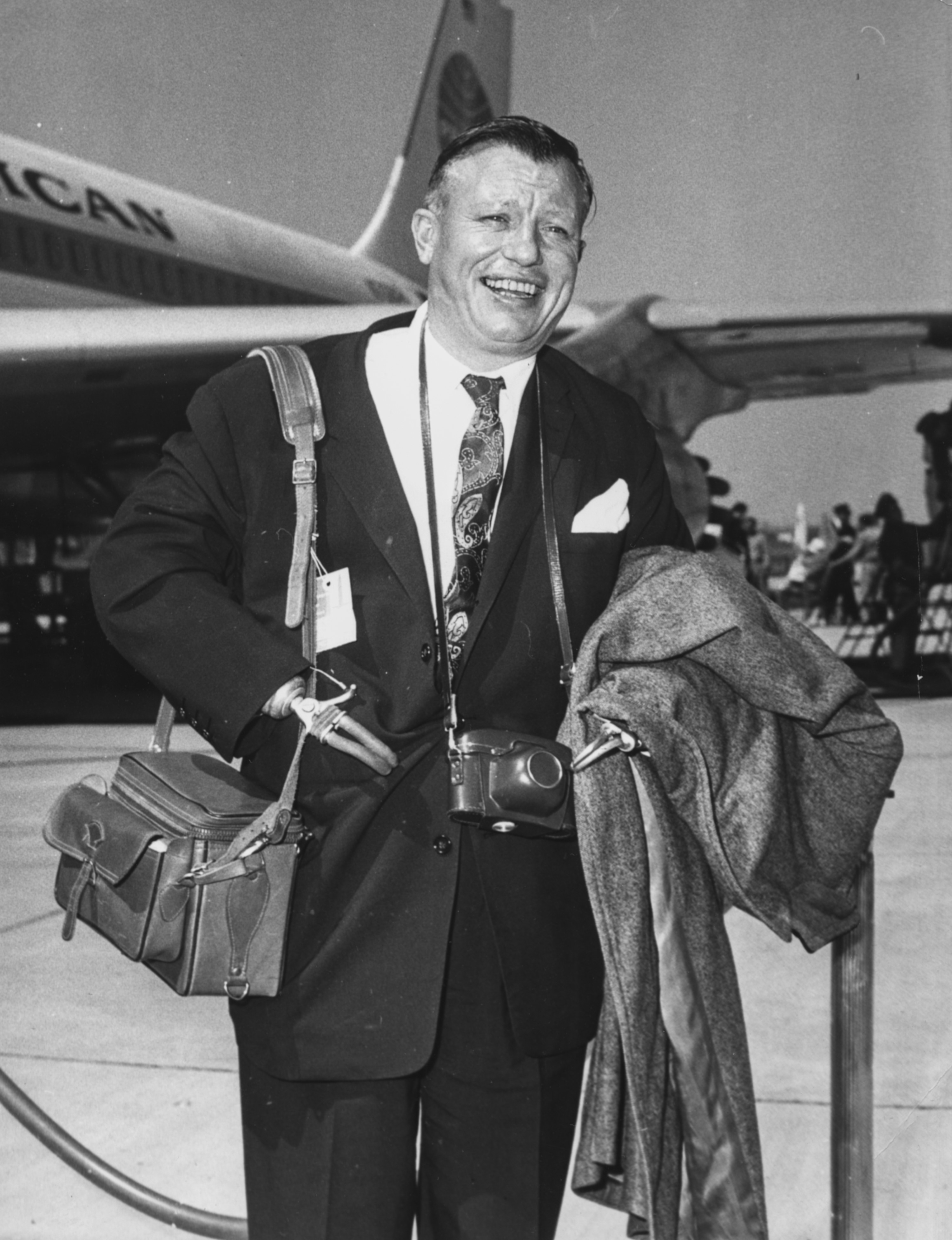 Harold Russell smiling and holding his luggage at an airport