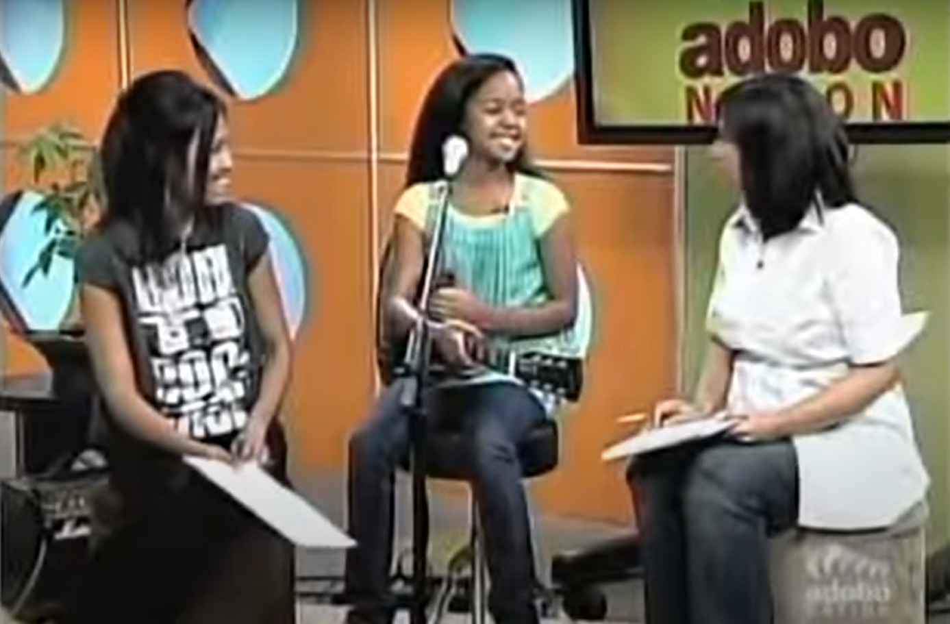 H.E.R. on Adobo Nation holding a guitar and being interviewed by two people when she was 11