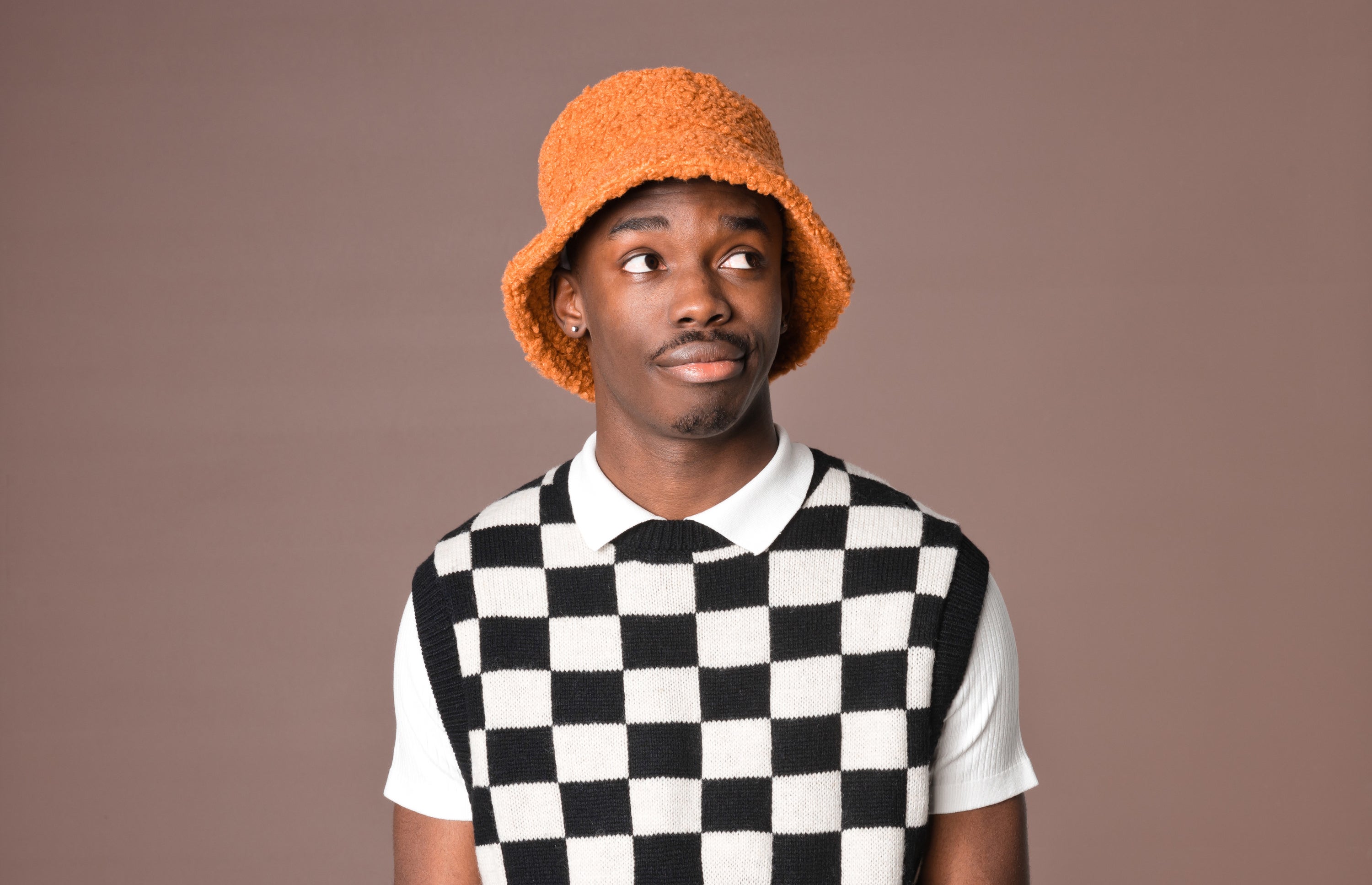 young man in black and white checkerboard vest and orange bucket hat