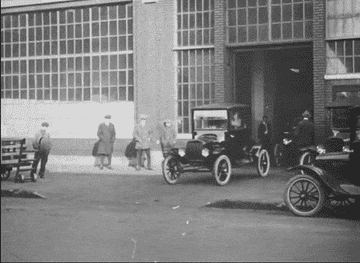 Model T cards drive out of a factory