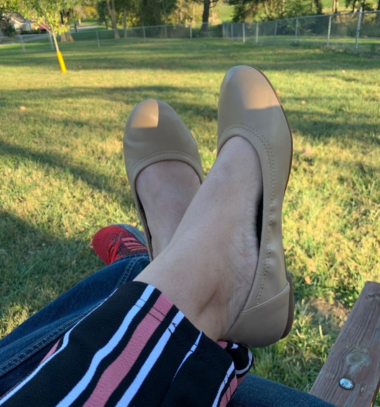 Reviewer with ankles crossed wearing beige flats and sitting outside on bench