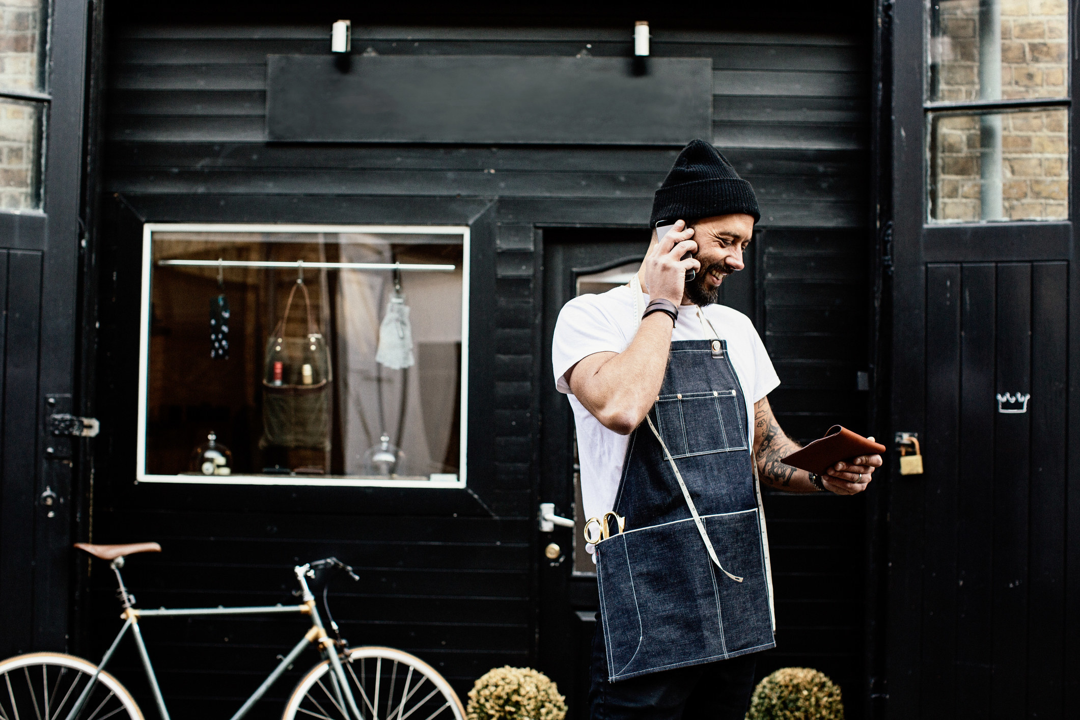 Worker outside a shop talking on a phone while looking at a tablet