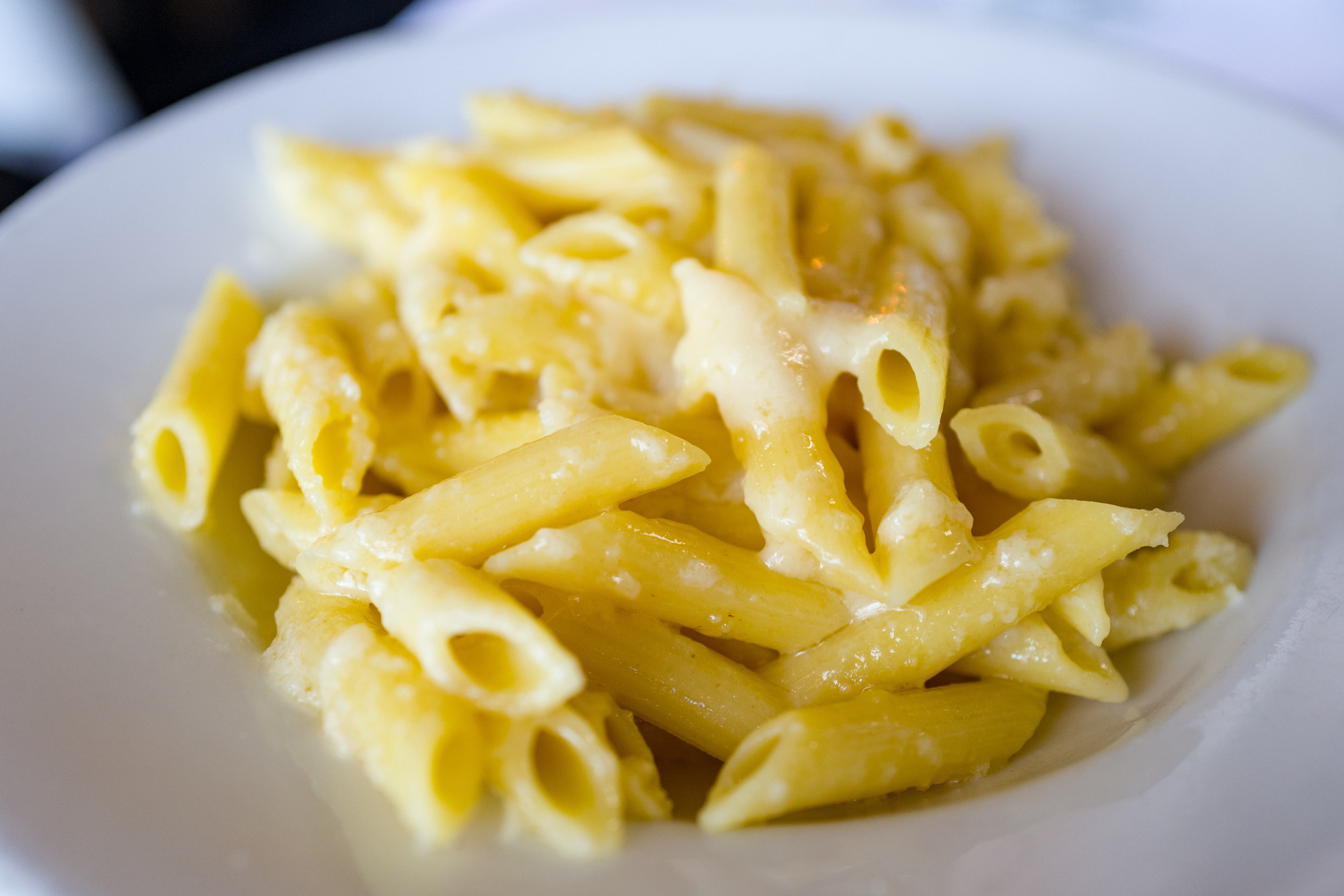 Close-up of penne pasta in a white bowl with melted Parmesan cheese and butter.