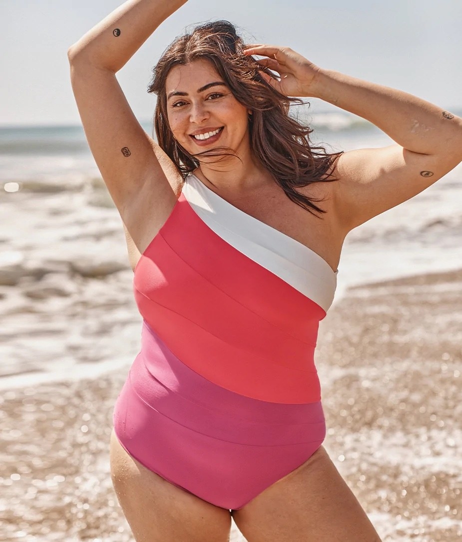 model in one shoulder one-piece in pink, coral, and white panels