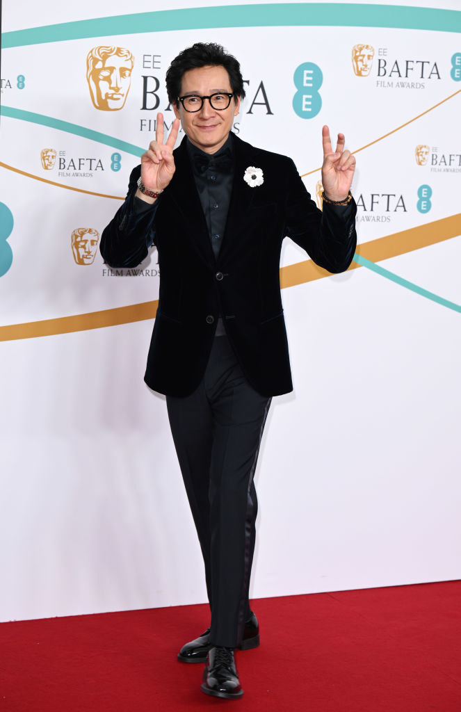 Ke Huy Quan attends the EE BAFTA Film Awards 2023 at The Royal Festival Hall in a velvet suit giving the peace sign