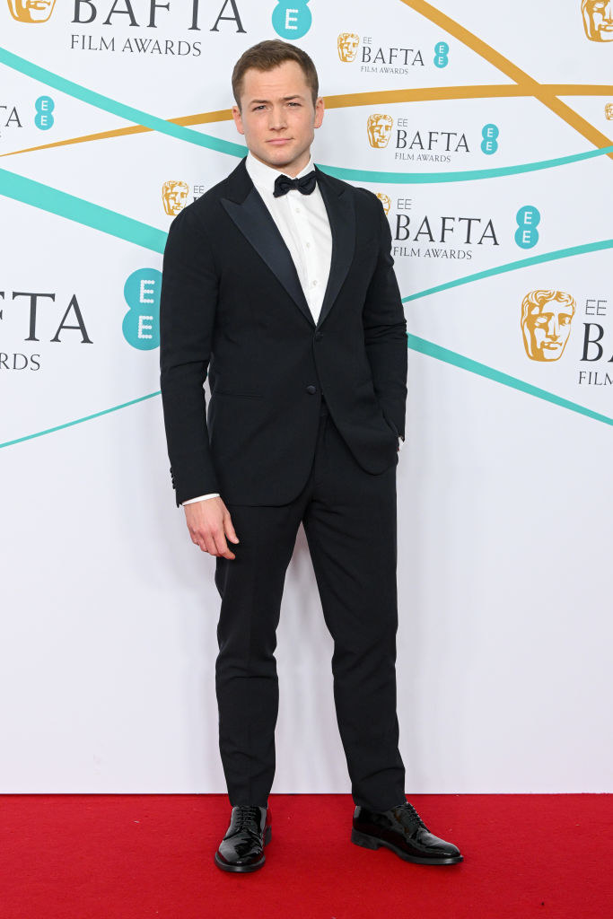 Taron Egerton attends the EE BAFTA Film Awards 2023 at The Royal Festival Hall in a traditional suit