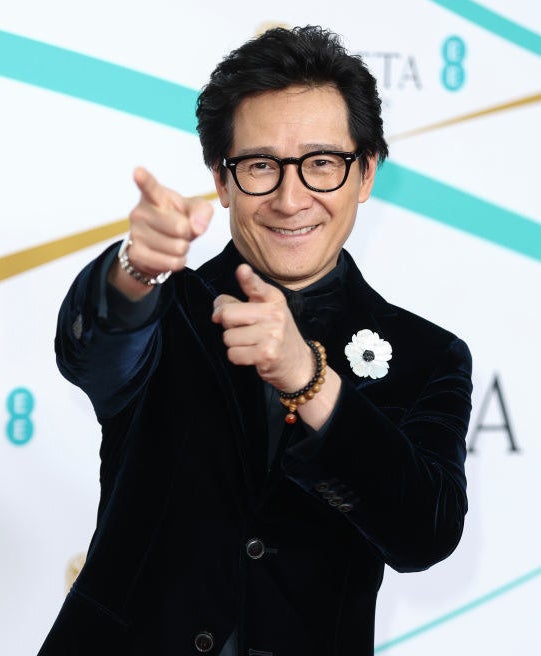 A closeup on Ke Huy Quan pointing towards the photographers on the red carpet
