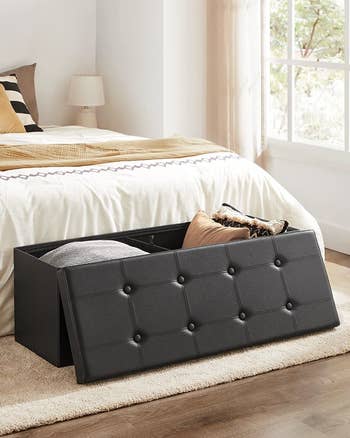 the black rectangular storage ottoman bench with the lid off and pillows stored inside