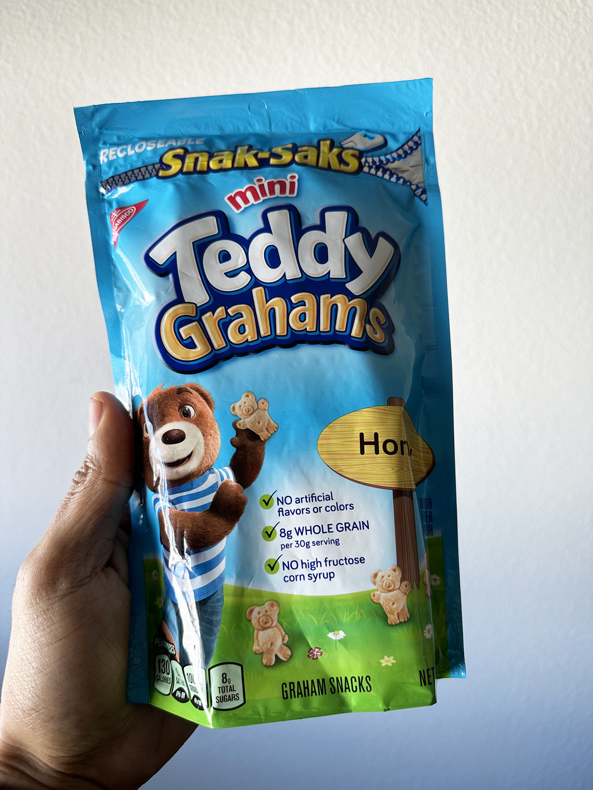 A hand holding a pack of Mini Teddy Grahams snacks