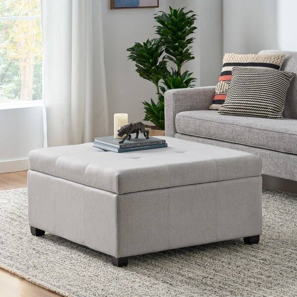 the large grey storage ottoman with books and decor on top in front of a couch