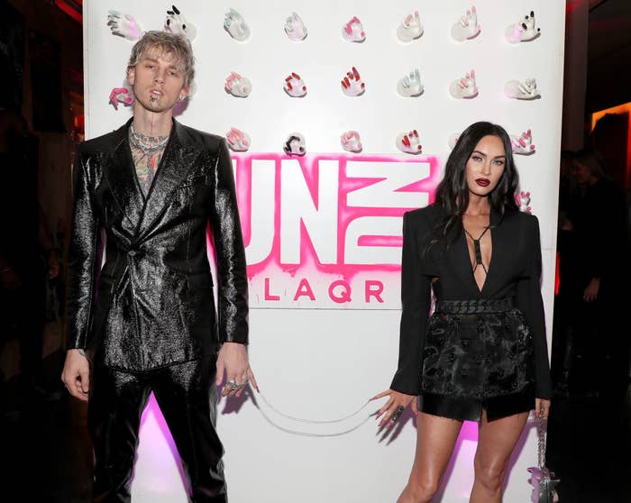 MGK posing at a red carpet event with allegedly off-again significant other Megan Fox attached at each other&#x27;s pinky fingers by a chain