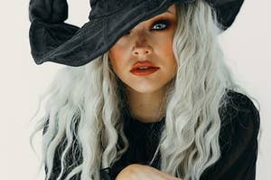 A woman with white hair and a witches hat stares at you.