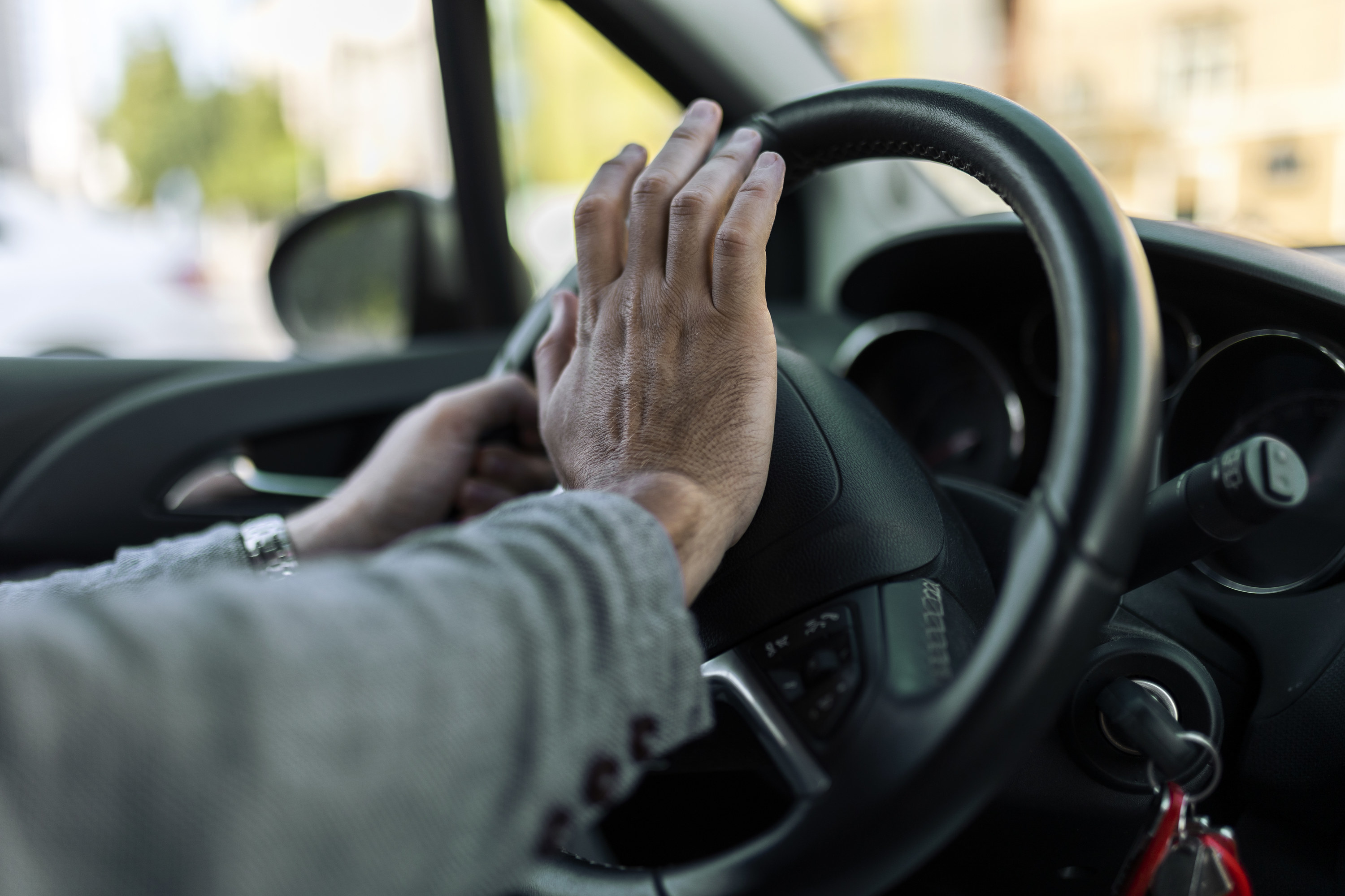 An image of a man&#x27;s hand honking a horn on a car steering wheel