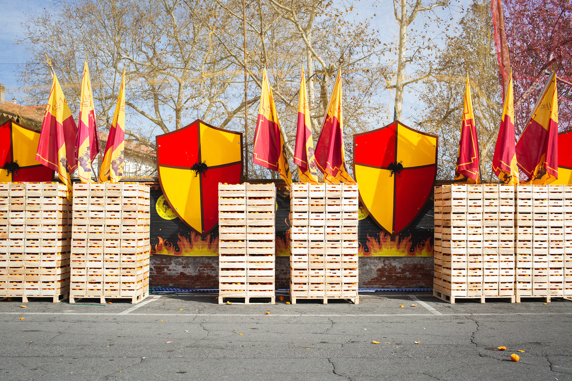 Six tall, vertical stacks of wooden crates of oranges sit in a parking lot in front of a coat of arms and flags depicting the team&#x27;s colors
