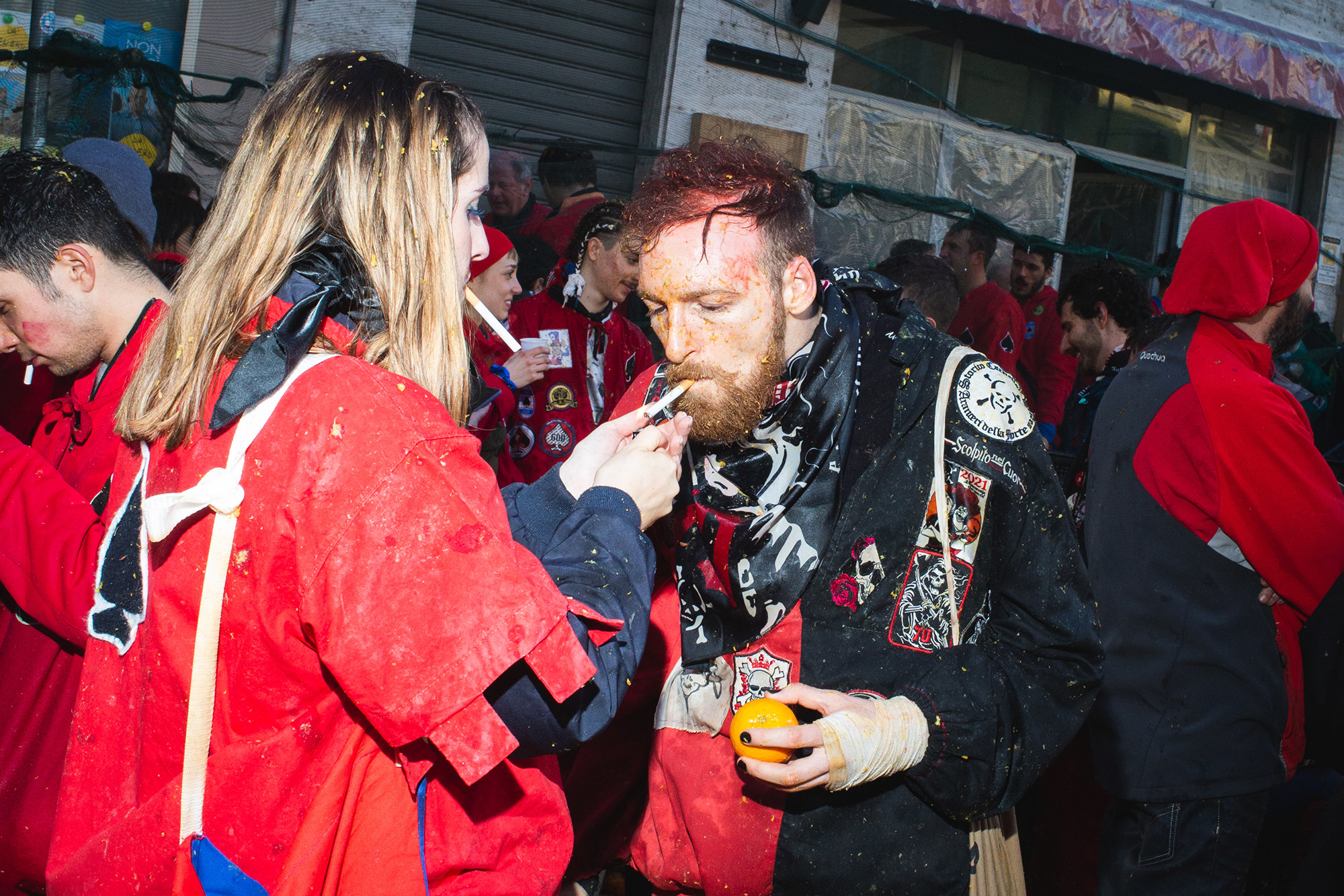 A woman lights a man&#x27;s cigarette; the man is holding an orange