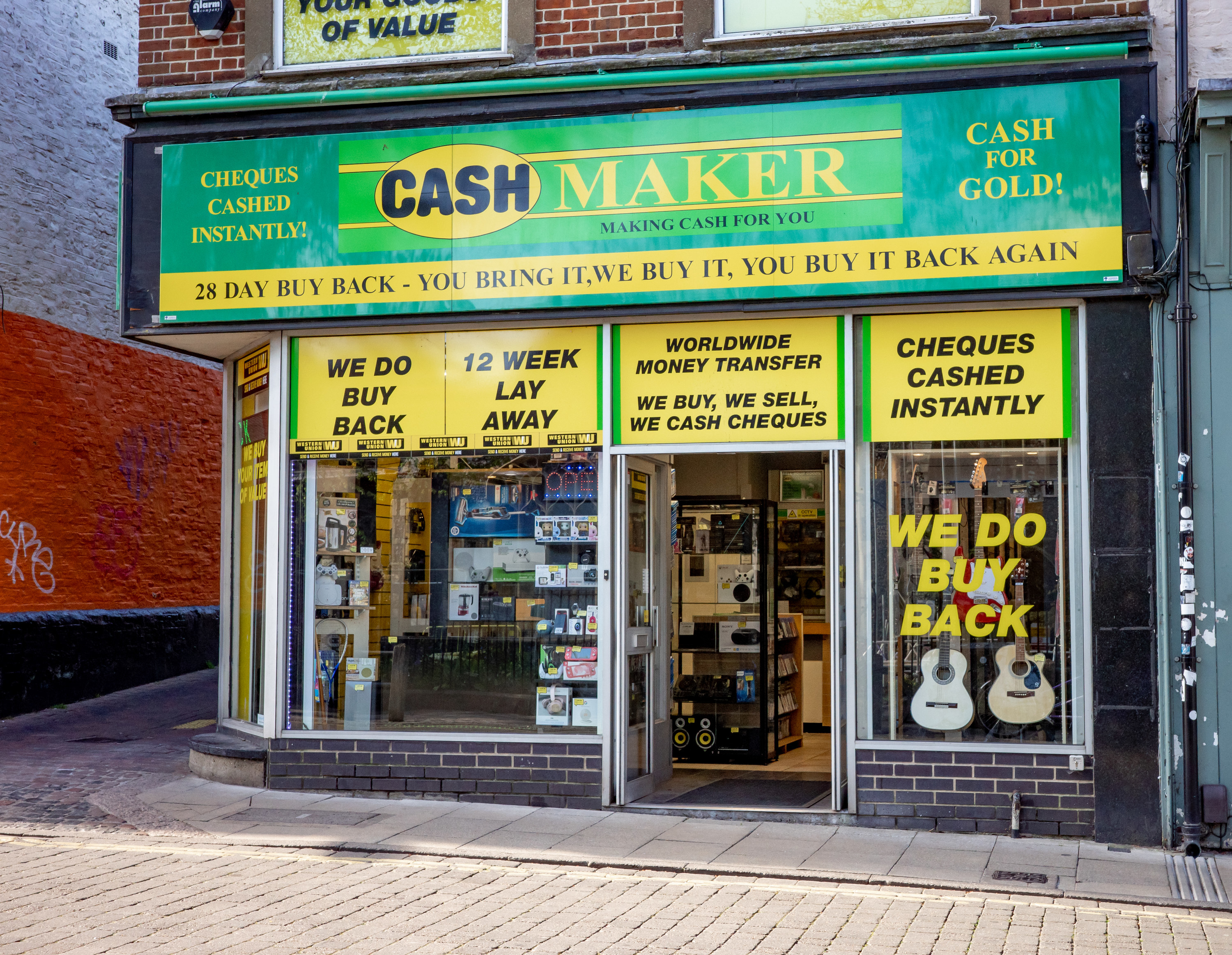 An image of a pawn shop with a green and yellow shop front with many signs, with things like &quot;We do buy back&quot; and &quot;cash for gold!&quot; written on them