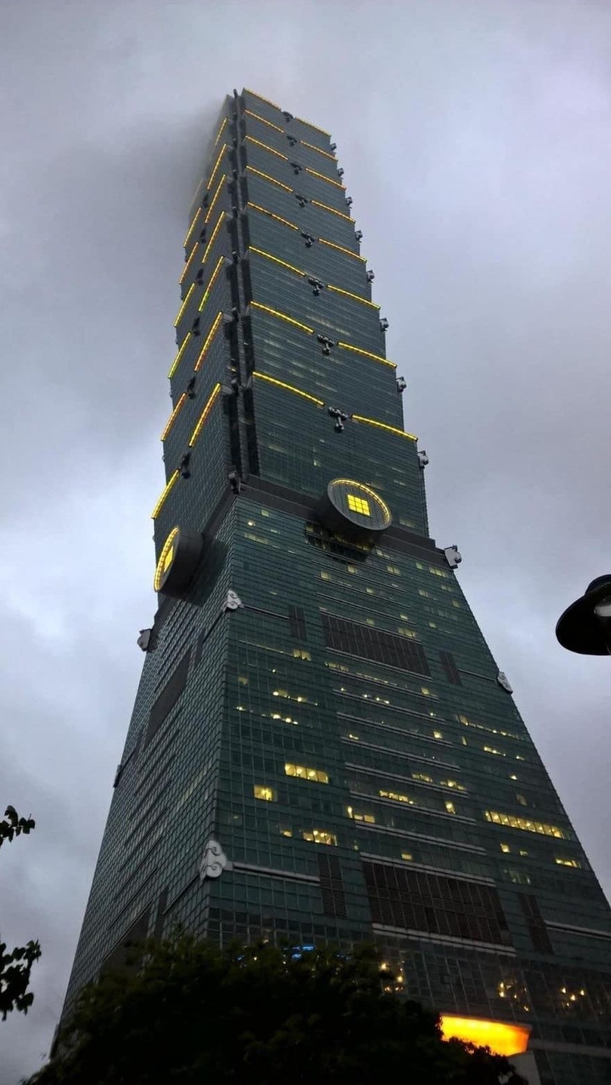 A very tall glass, city tower building that is dark, with only slivers of yellow lights
