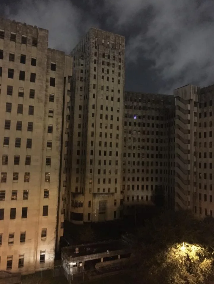 a massive building with 12 floors that looks abandoned, except for one small window with a light on