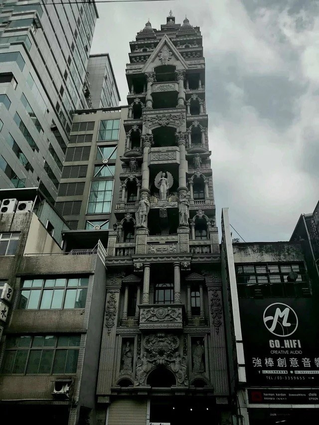 A narrow but tall building that has many sculptures and carved details that look like winged creatures