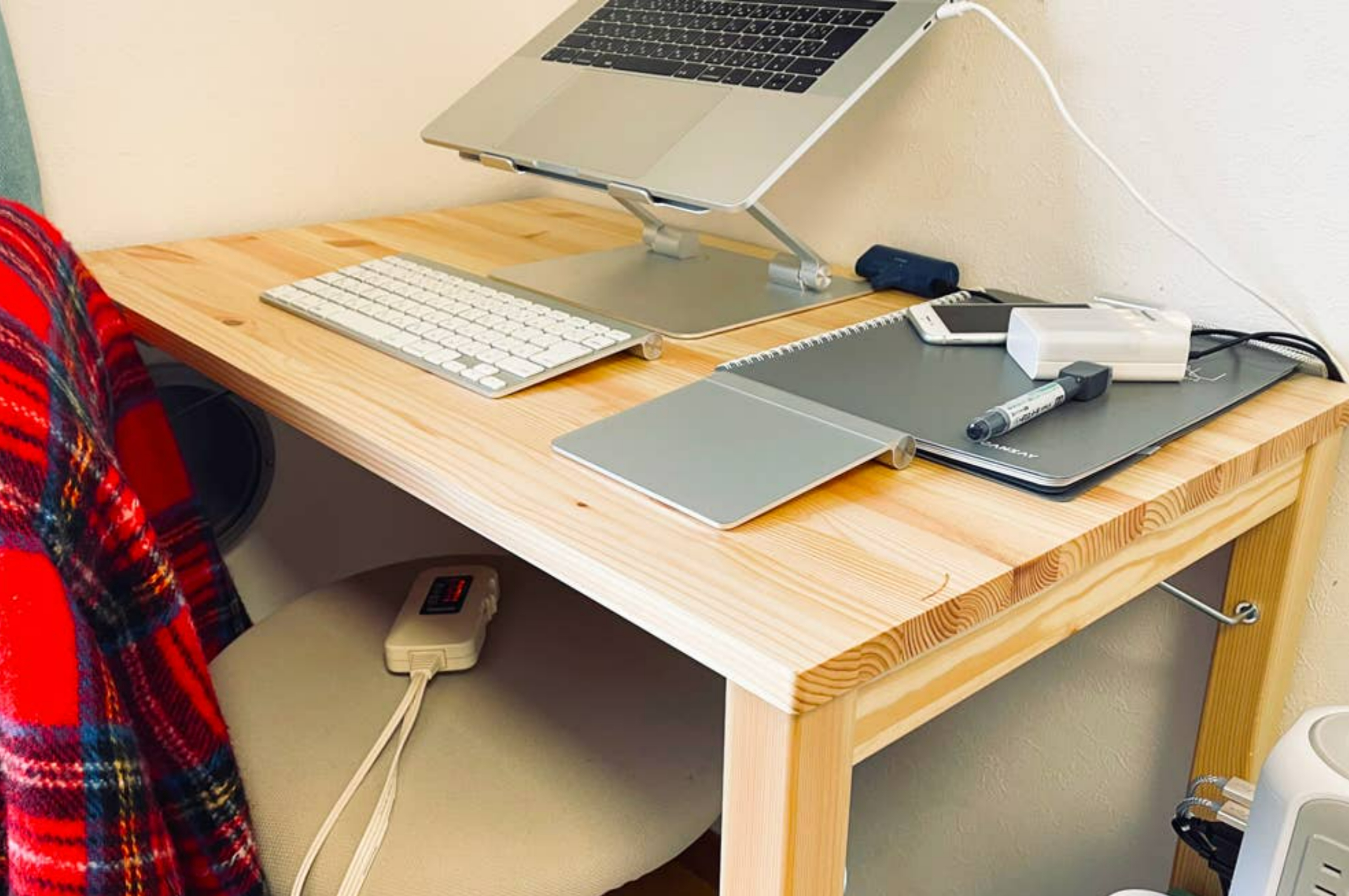 ノートパソコンとキーボードが置かれたデスク。デスク上にはノートとペンがあり、椅子にはブランケットがかけられている。