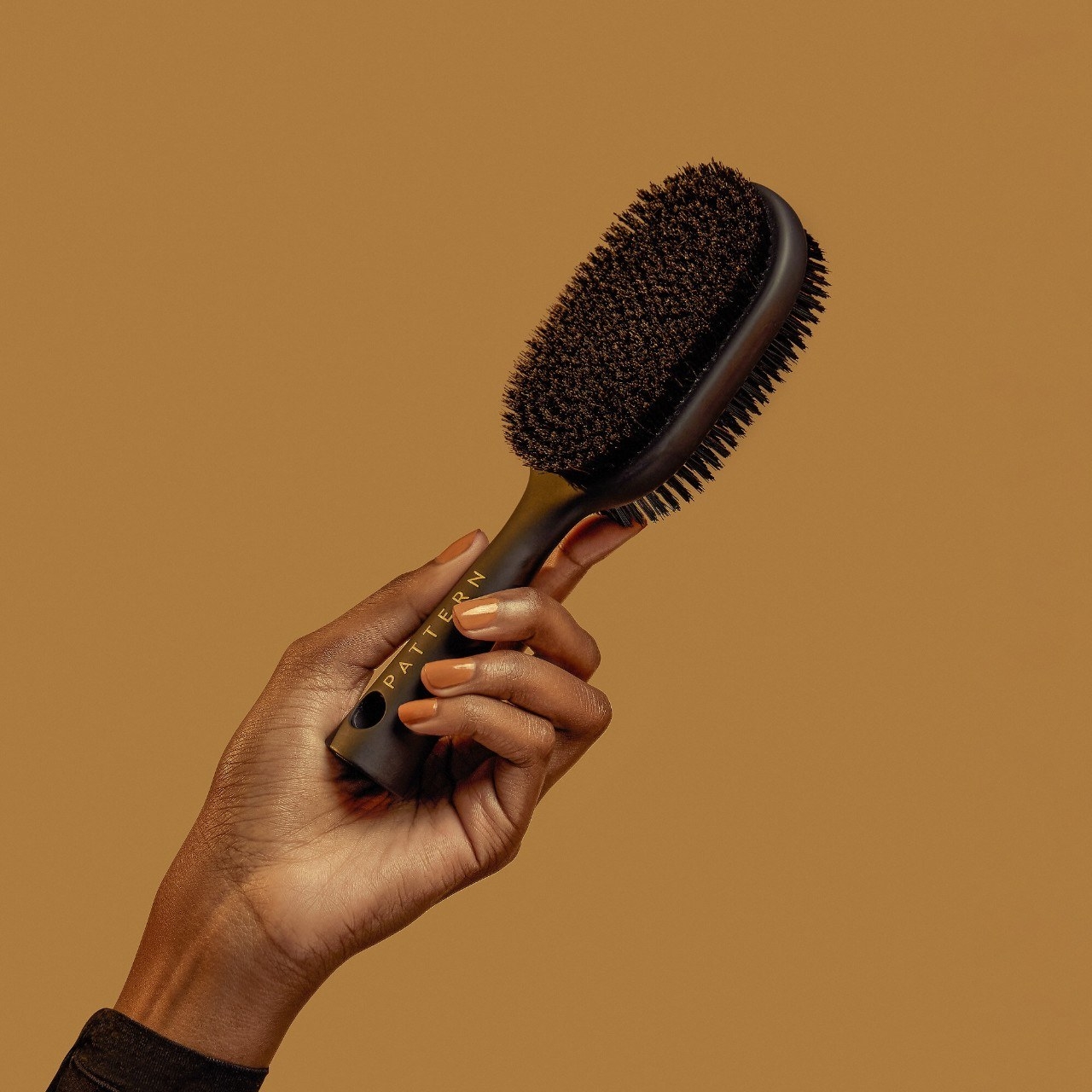 someone holding up the two-sided brush; one side has longer nylon bristles and the other shorter, denser boar hair bristles