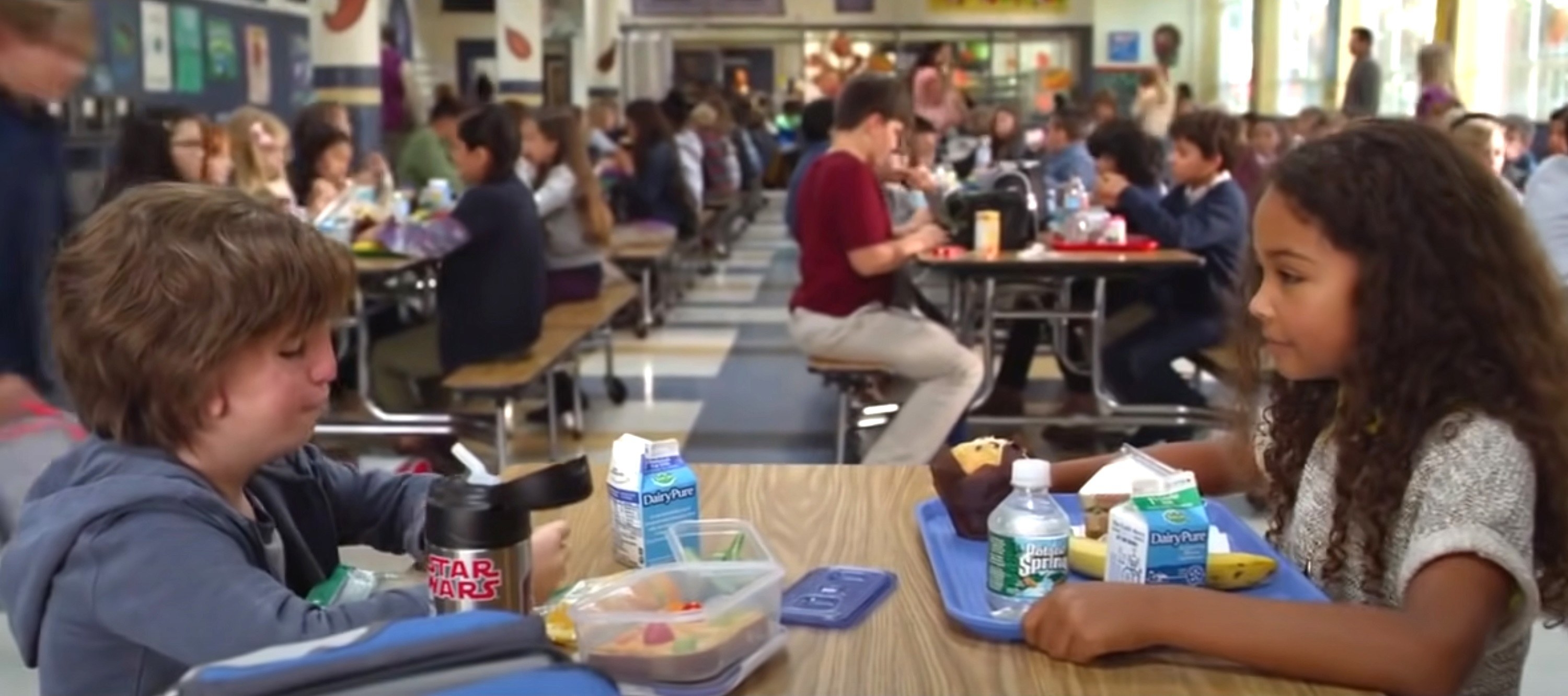 Two children sit at a table in a school cafeteria