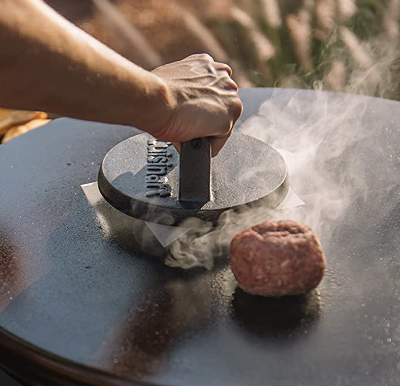 a person using the burger press on a patty on a grill