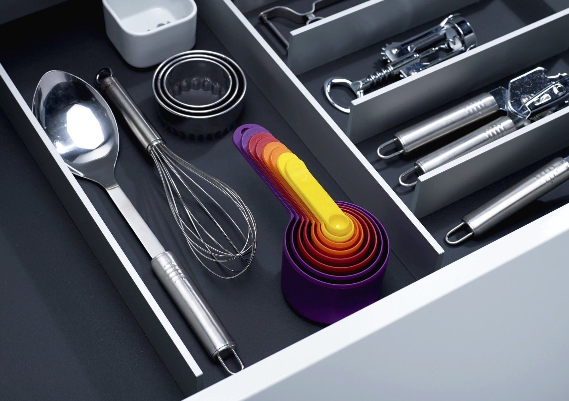 The nesting, multi-colored measuring cups in a drawer with other utensils