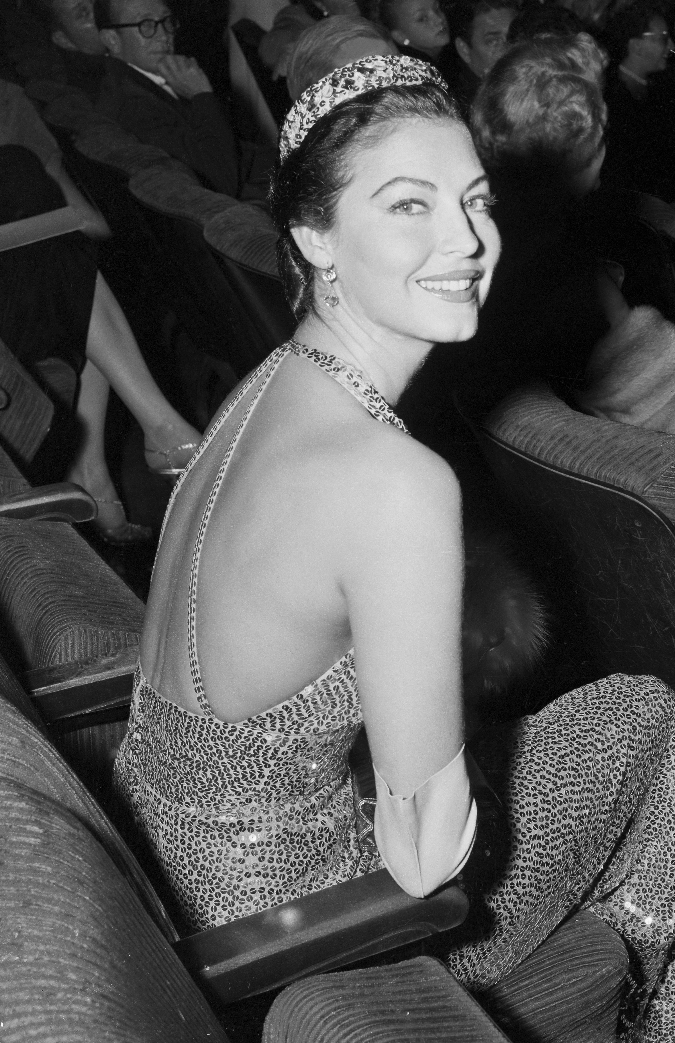 Ava Gardner looking over her shoulder in a gown while sitting in a movie theater seat