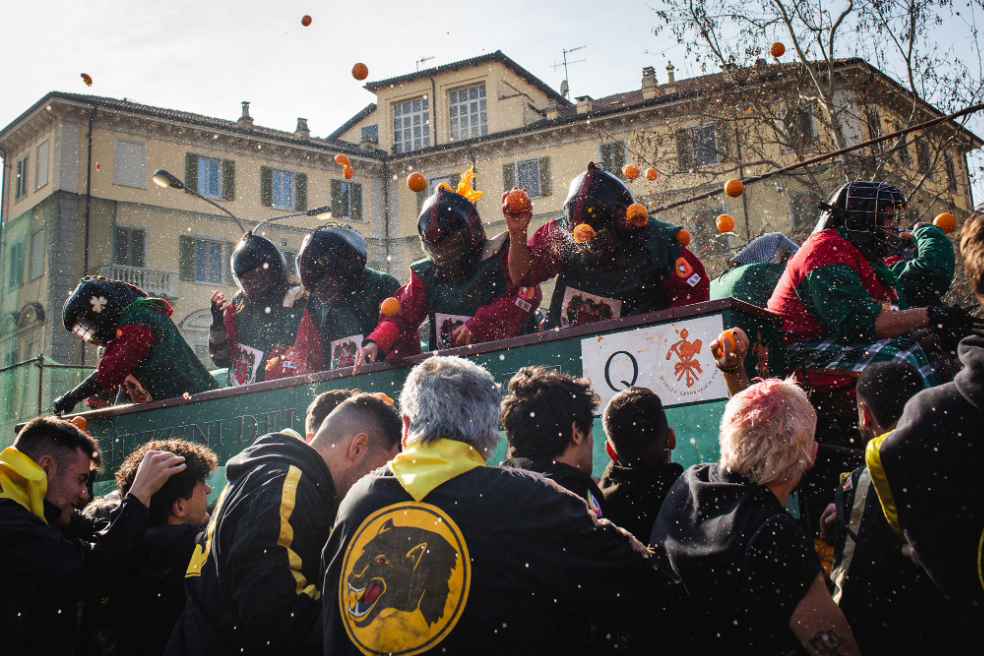 people in medieval soldier garb throw oranges and pelt onlookers from a raised cart