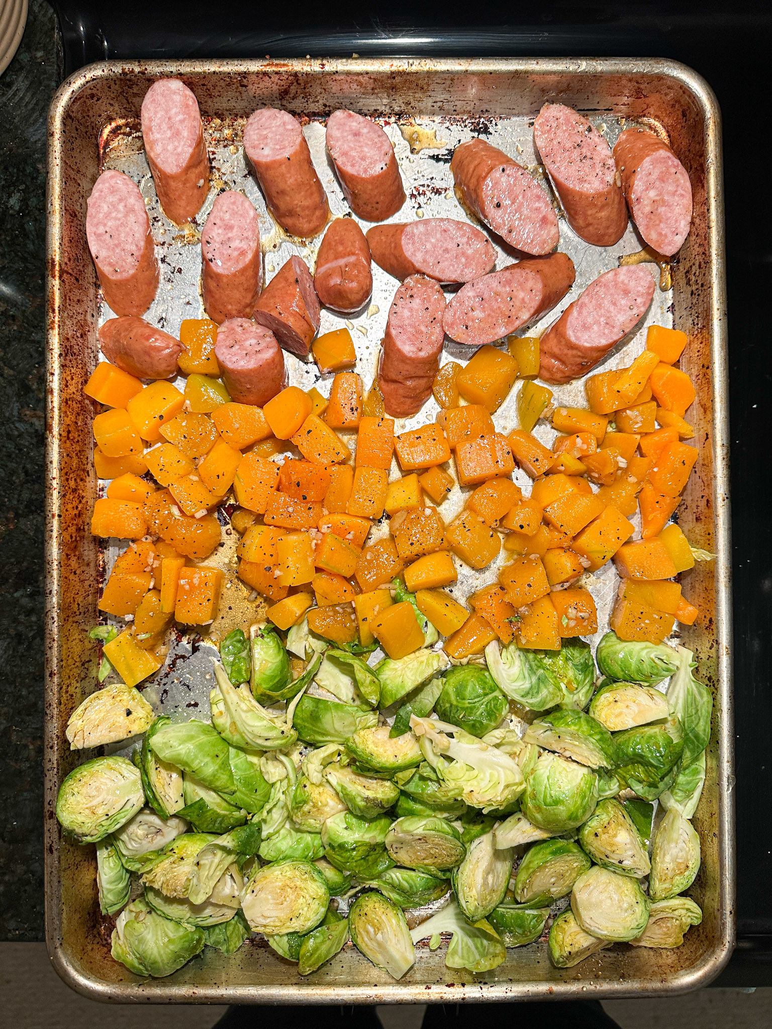 sausage, squash, and brussels sprouts all lined up and seasoned on a sheet pan