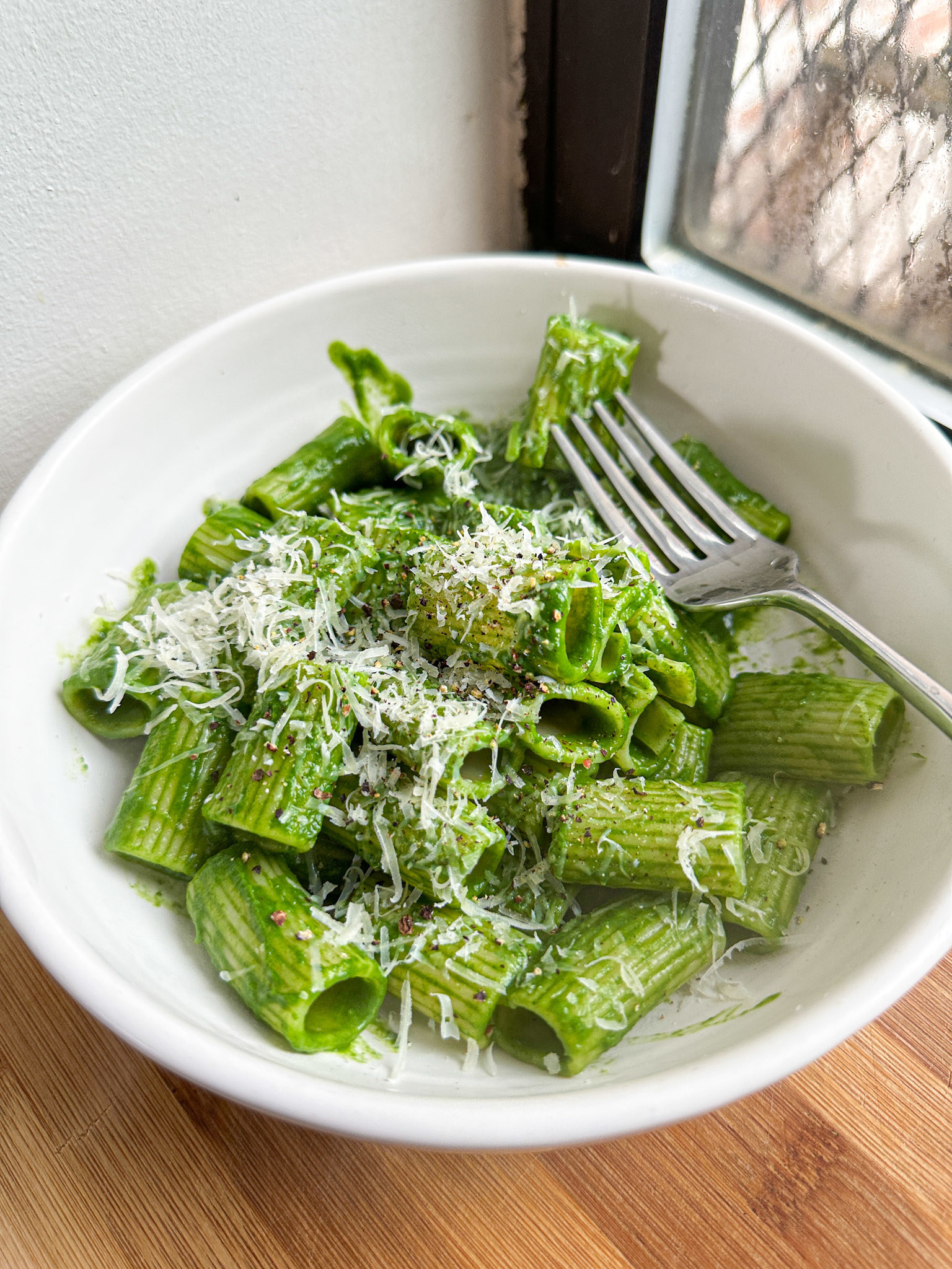 rigatoni pasta coated in a vibrant green sauce with parmesan cheese and black pepper
