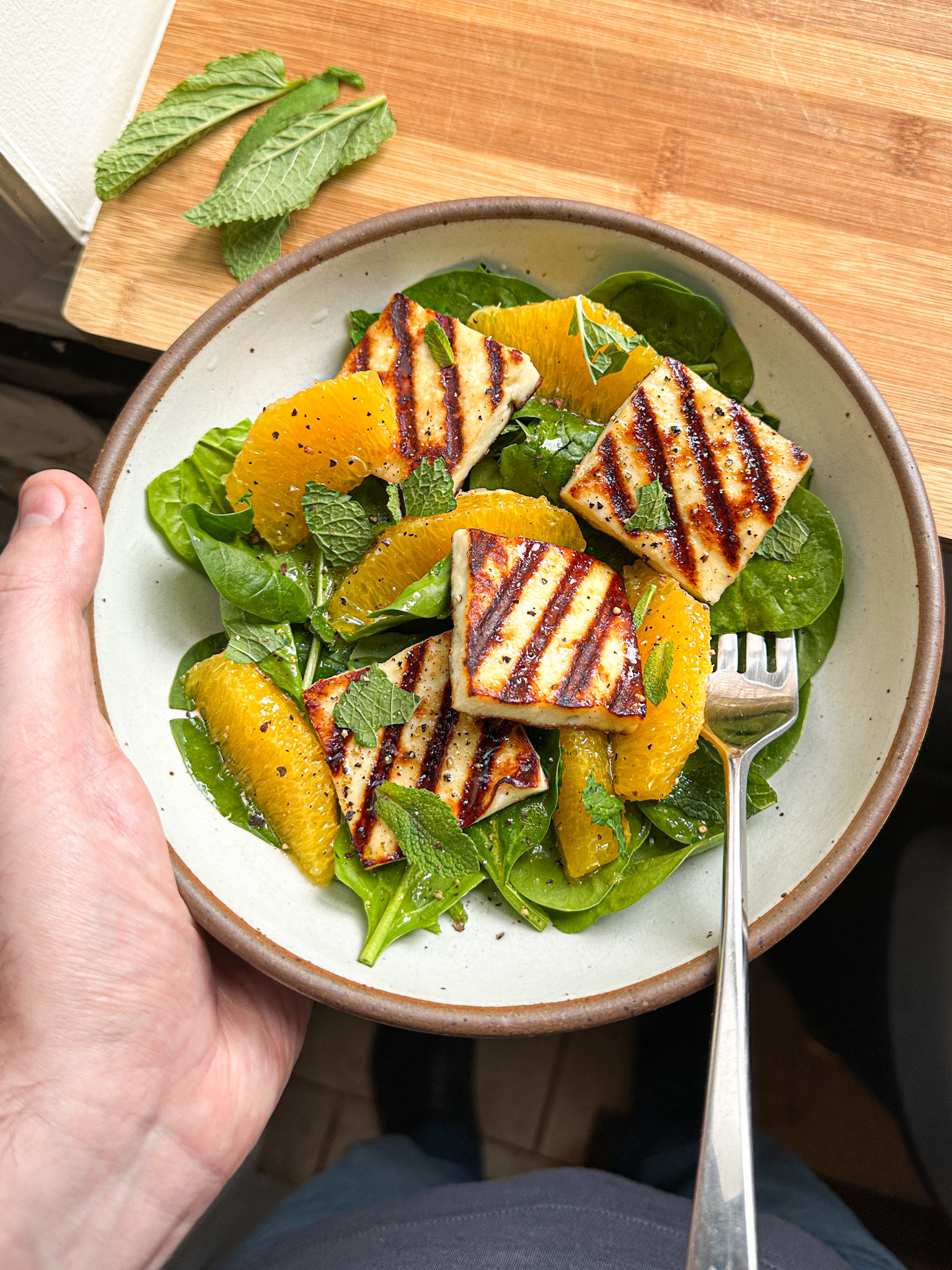 bowl of baby spinach salad topped with the pan fried cheese with diagonal grill marks, and orange segments