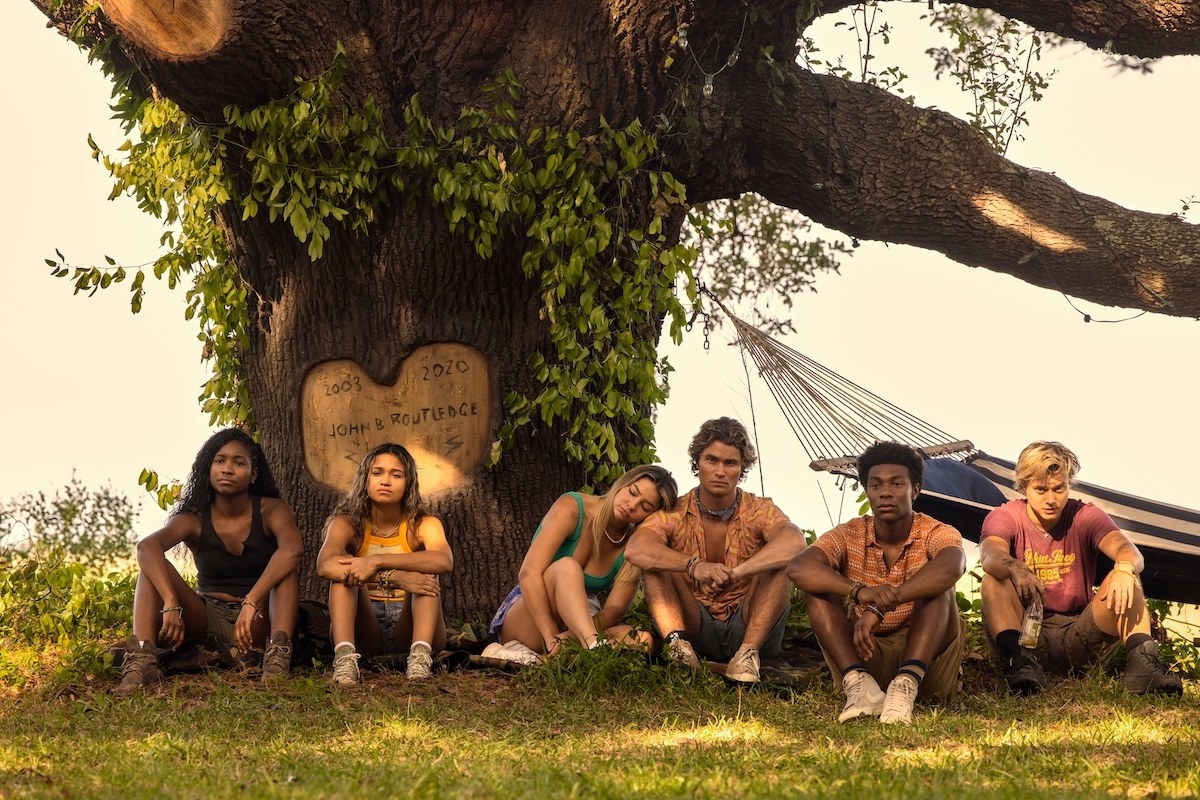 The cast sitting in the grass in front of a hammock in a scene from the series