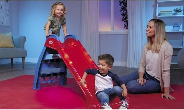 Two kids playing on the slide with a parent watching