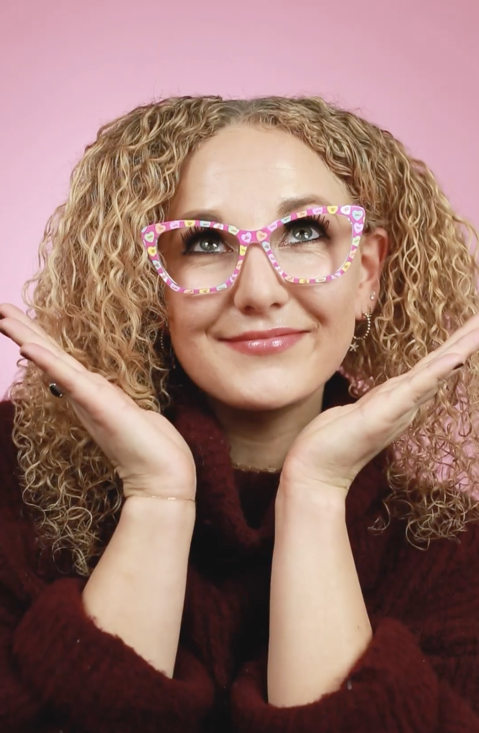person with their hands open framing their face and the pair eyewear candy heart design frame on