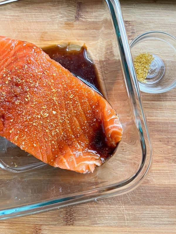 salmon in a glass dish with sauce and seasoned salt sprinkled overtop