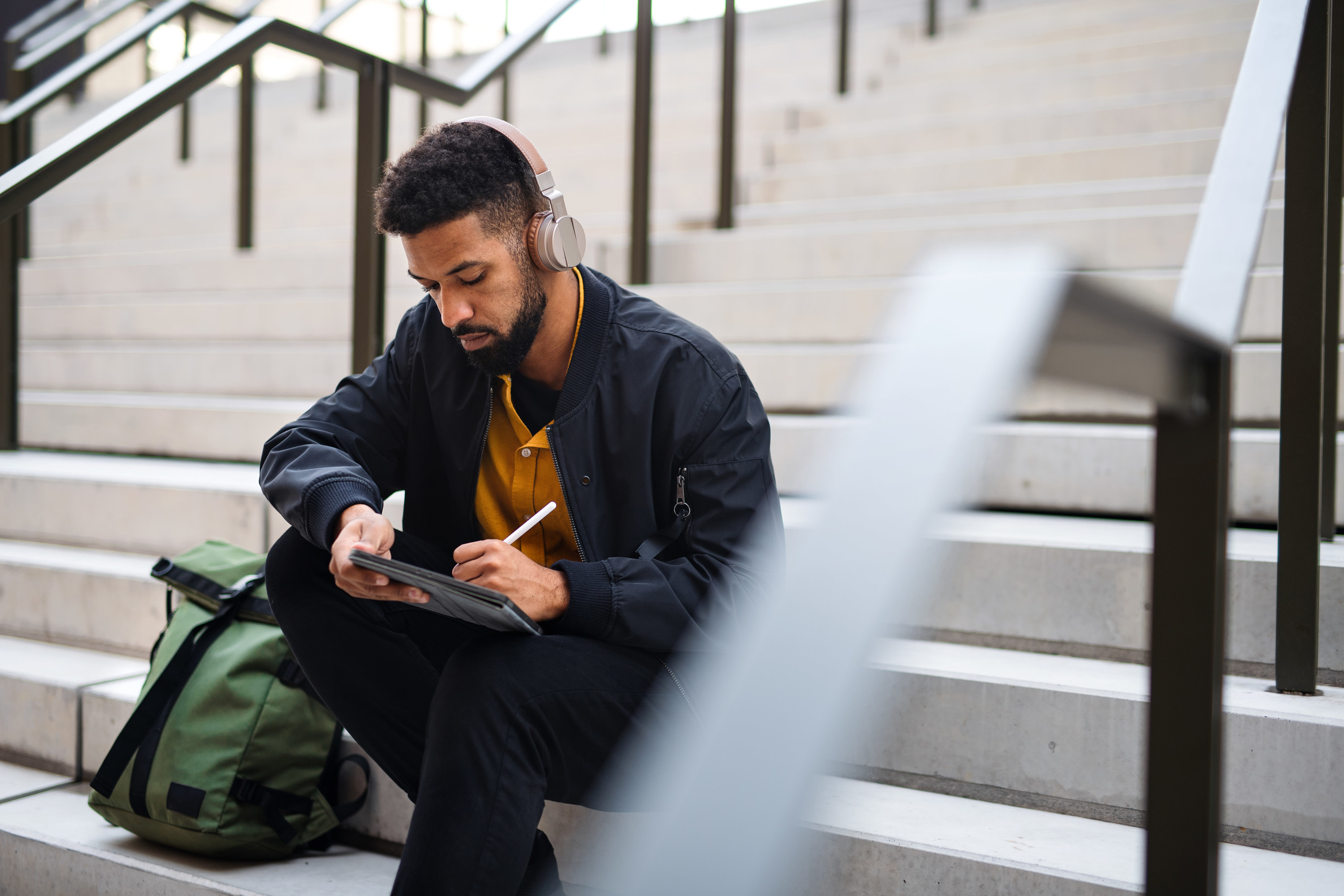 a man sitting on steps writing in a notebook with headphones on