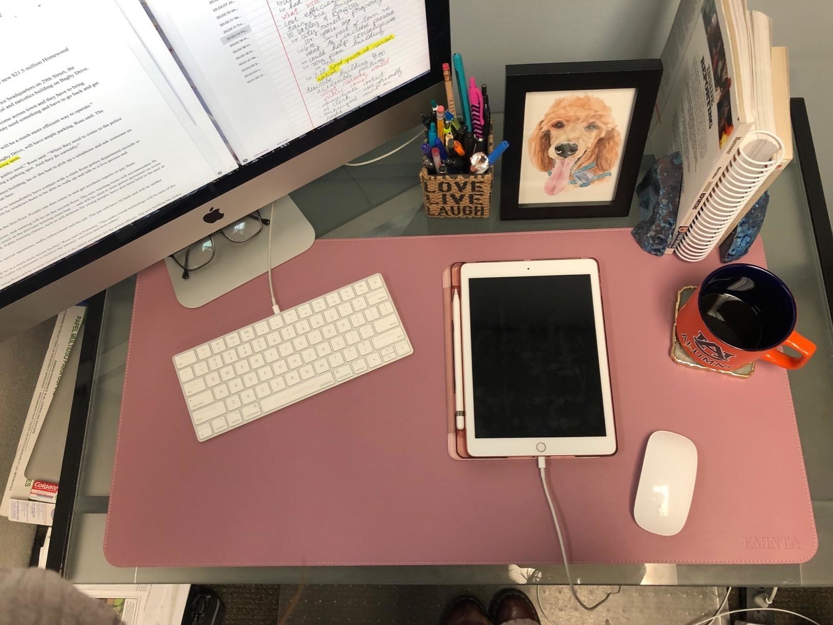 pink desk mat on a desk with a keyboard, ipad, and other supplies on it