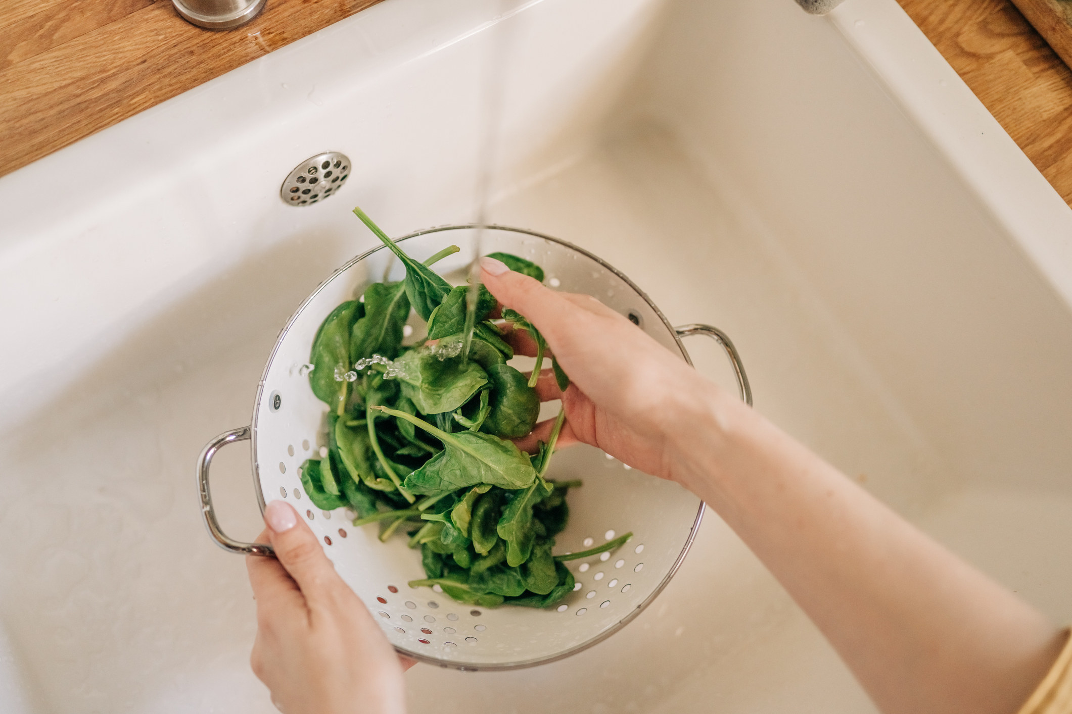 Hands washing spinach in sink.