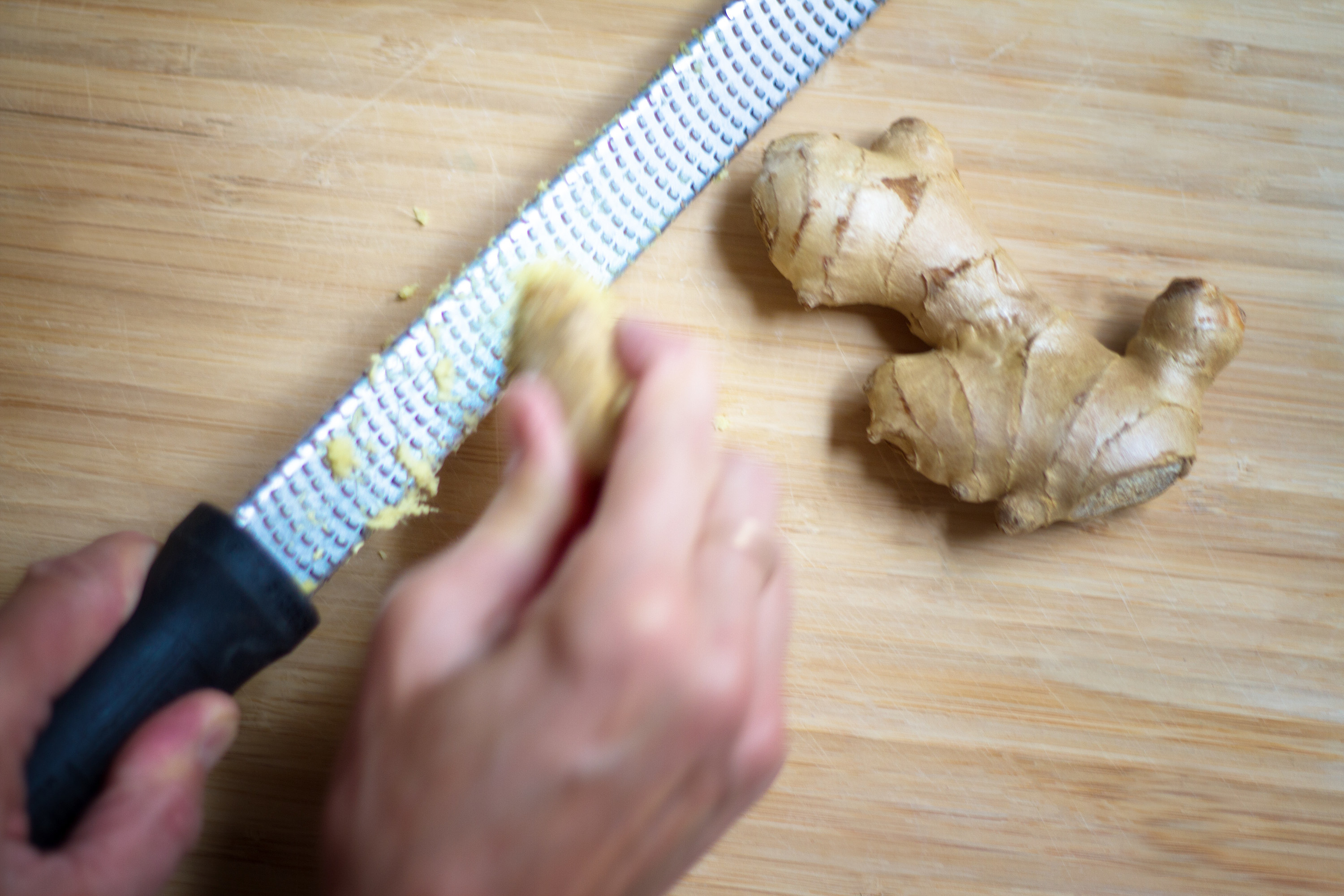 Hands grating ginger with a microplane.