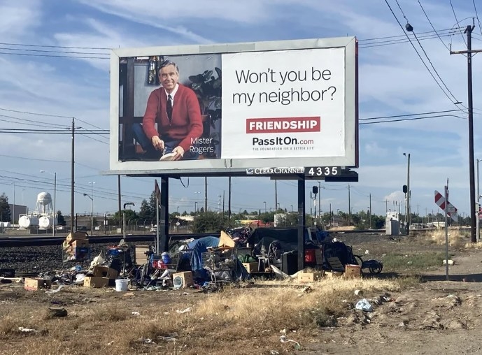 A billboard of Mr Rogers advocating for friendship over an unhoused encampment