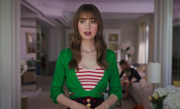 Emily wears a green and red outfit with a stunned expression on her face