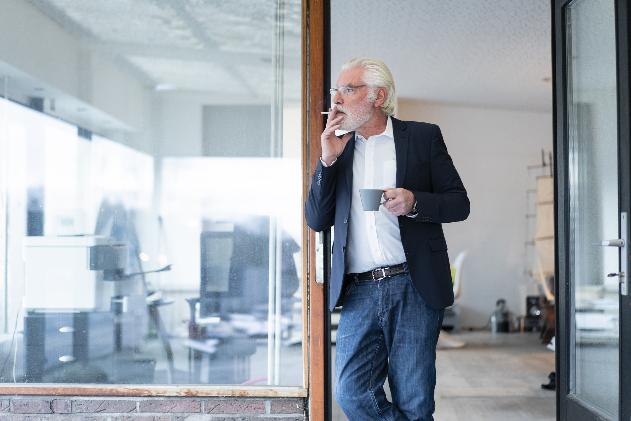 Man standing in a doorway smoking and holding a mug