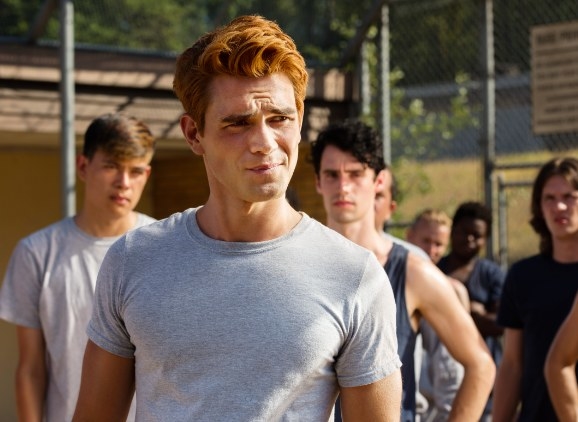 Archie wears a grey t-shirt and stands in front of a group of boys