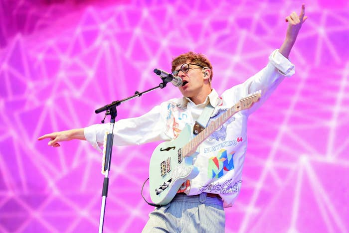Dave Bayley of Glass Animals flings his arms open while performing before a pink backdrop