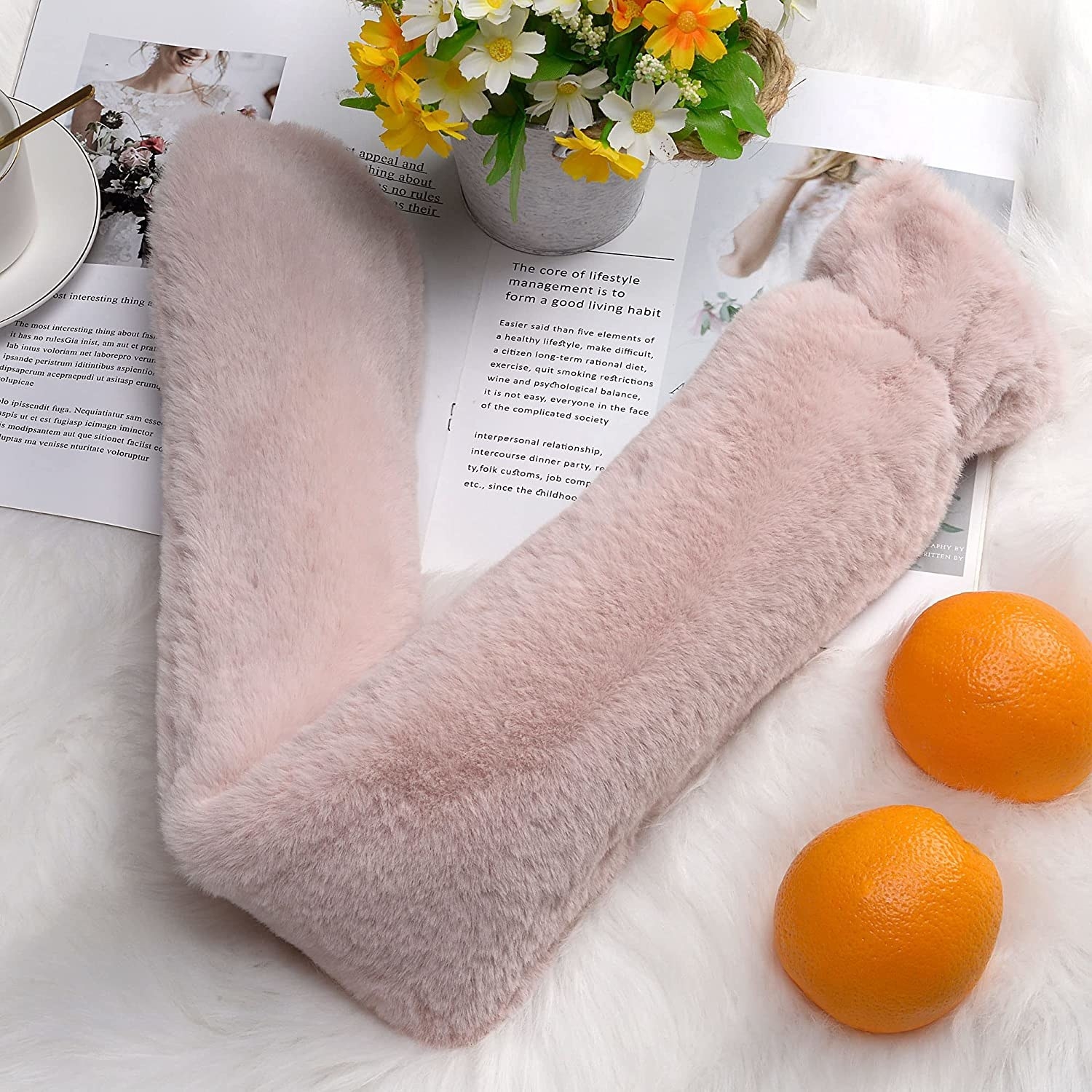 The hot water bottle on a fluffy rug surrounded by a plant and oranges