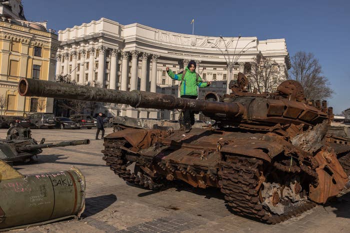 A boy in a green jacket climbs a destroyed Russian tank on display in a city center in downtown Kyiv