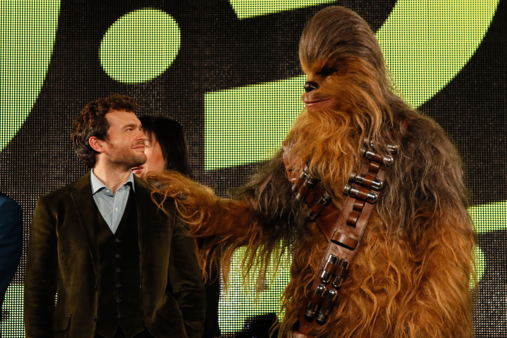 alden ehrenreich smiling up at chewbaca while chewbaca has a paw on his shoulder