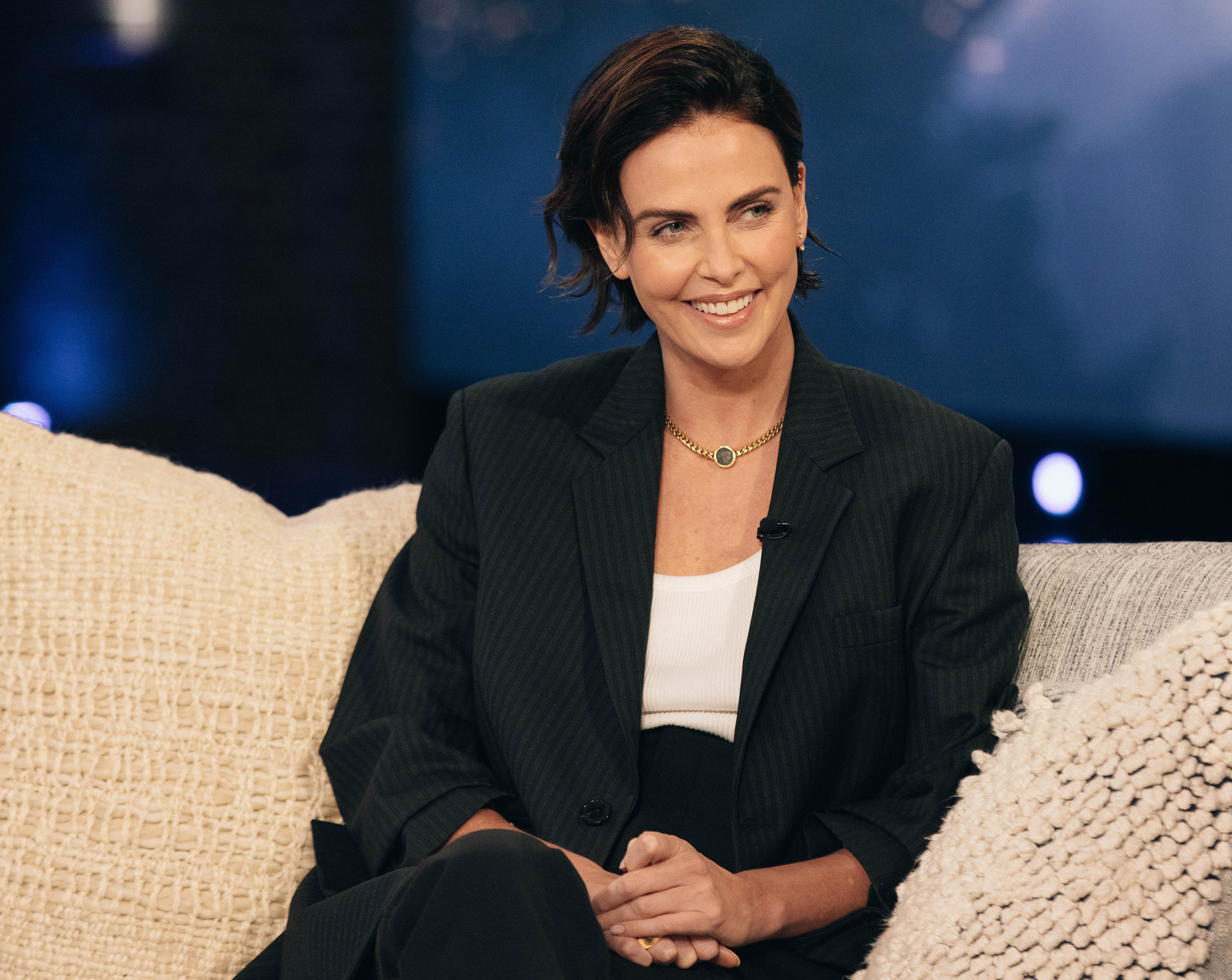 charlize theron smiling while sitting on a couch